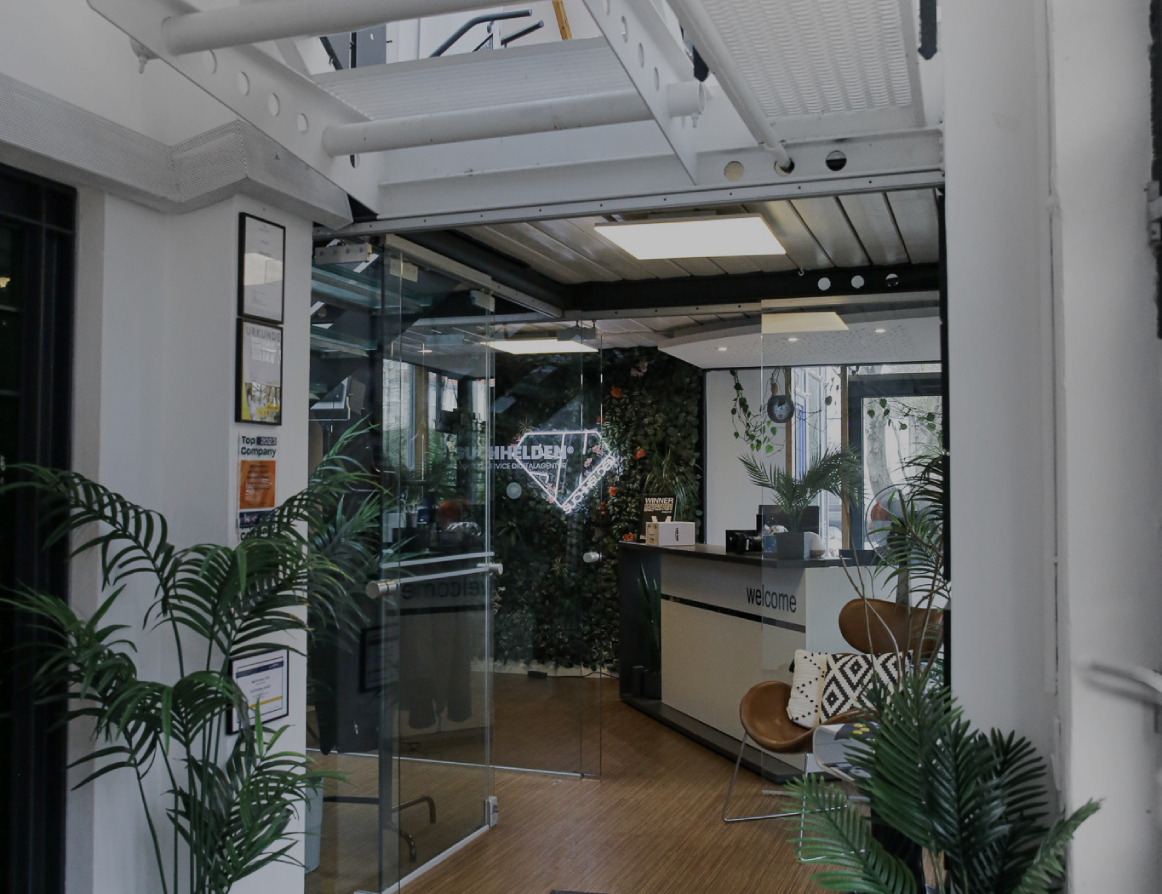 Eingangsbereich eines modernen Bürogebäudes mit Glas_tür, Empfangstresen, Pflanzen und offener Treppenkonstruktion