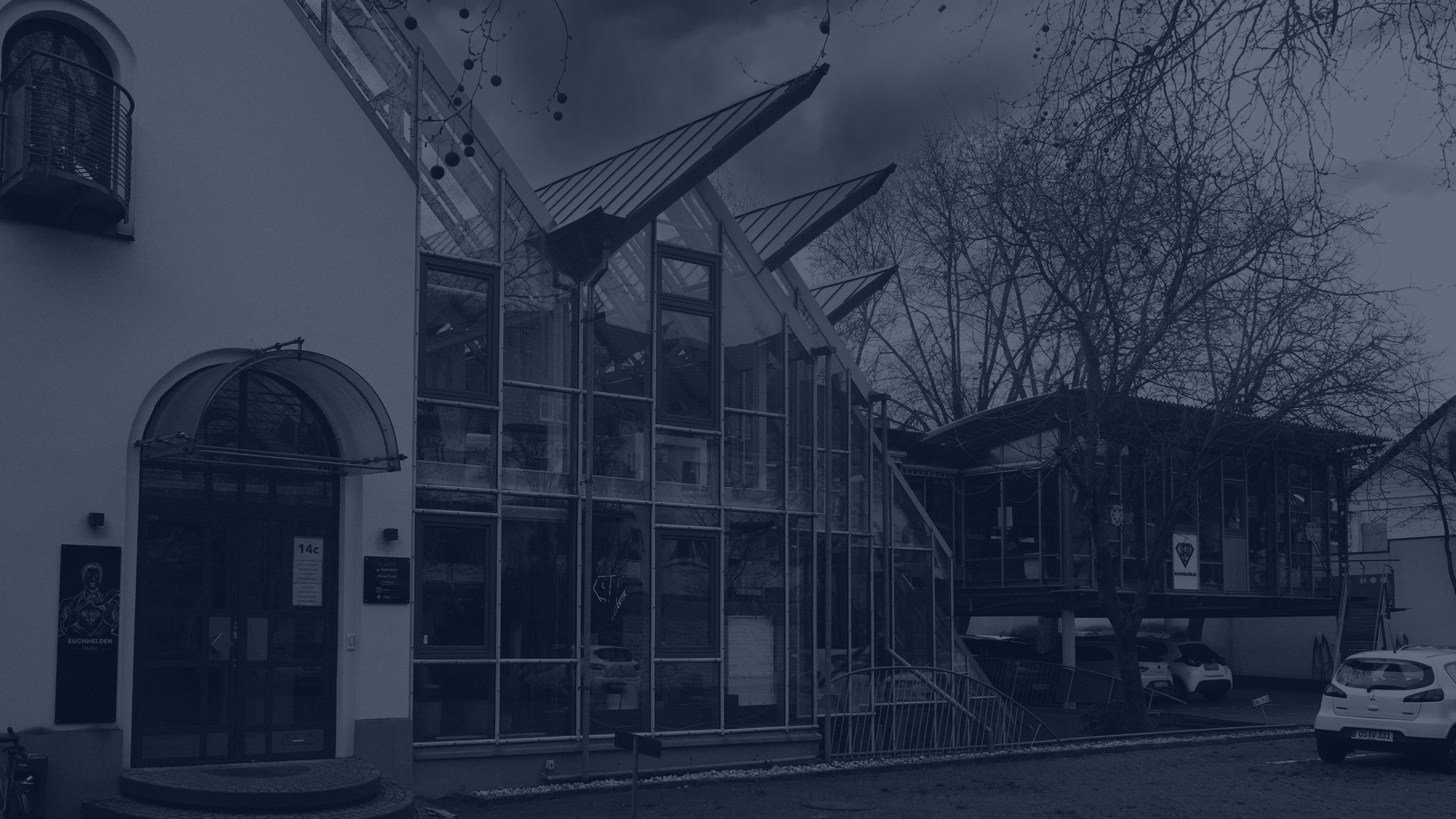 Modernes Bürogebäude mit Glasfassade und schrägen Dachflächen neben einem Innenhof mit parkenden Autos