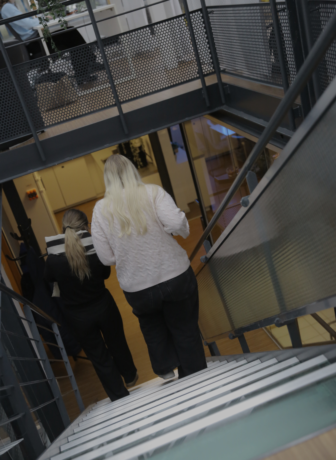Zwei Personen gehen eine Treppe in einem modernen Bürogebäude hinunter, aufgenommen von hinten