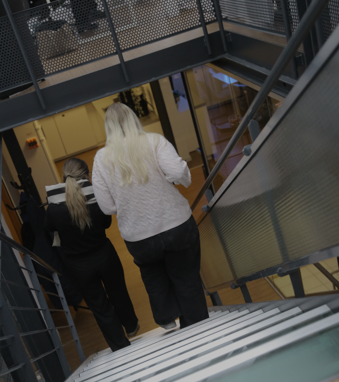 Zwei Personen gehen eine Treppe in einem modernen Bürogebäude hinunter, aufgenommen von hinten
