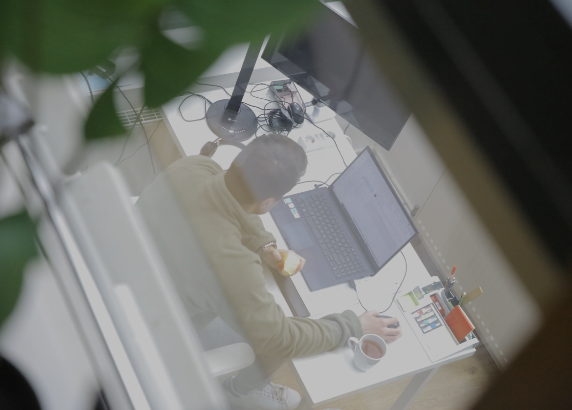 Person arbeitet an einem Laptop am Schreibtisch im Büro, hält einen Apfel in der Hand, aufgenommen aus erhöhter Perspektive