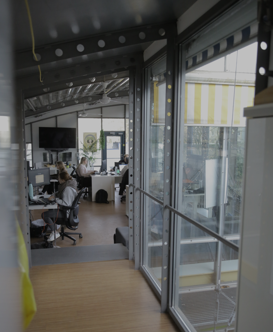 Blick durch eine Glaswand in ein Büro, in dem mehrere Personen an Schreibtischen arbeiten.
