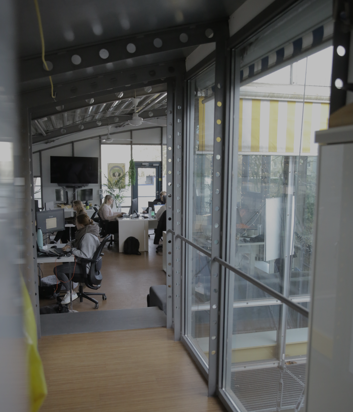Blick durch eine Glaswand in ein Büro, in dem mehrere Personen an Schreibtischen arbeiten.