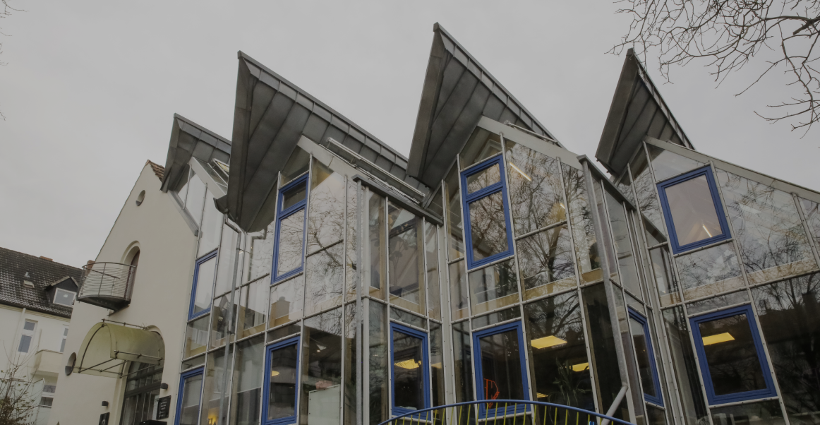 Aussenansicht eines modernen Glasgebäudes mit blauen Fensterrahmen und schrägem Dach 