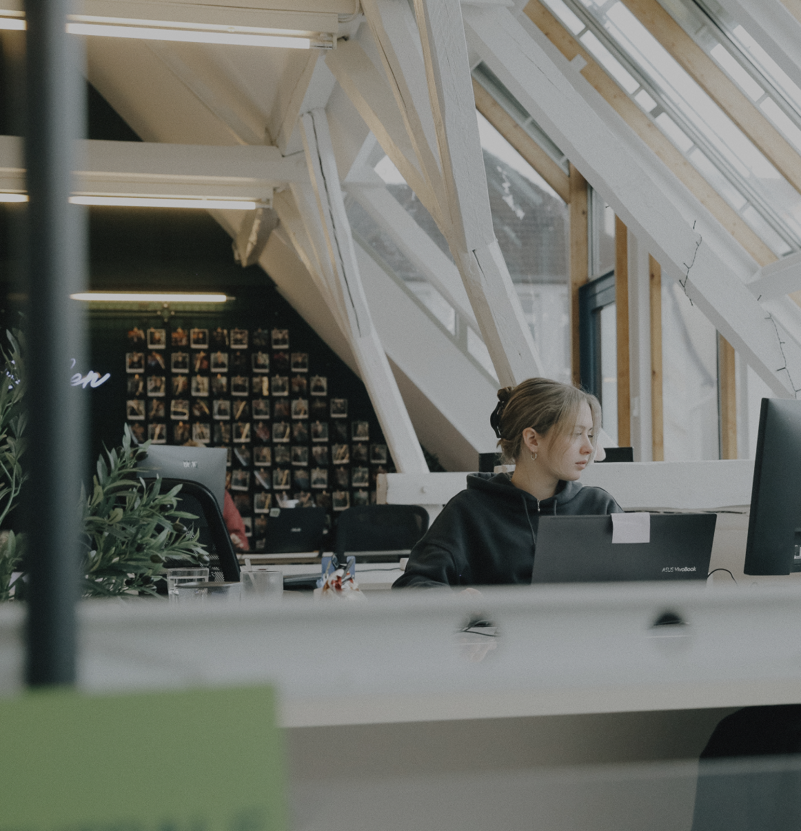 Person arbeitet konzentriert an einem Laptop in einem hellen Büro mit schrägen Dachfenstern und Holzbalken