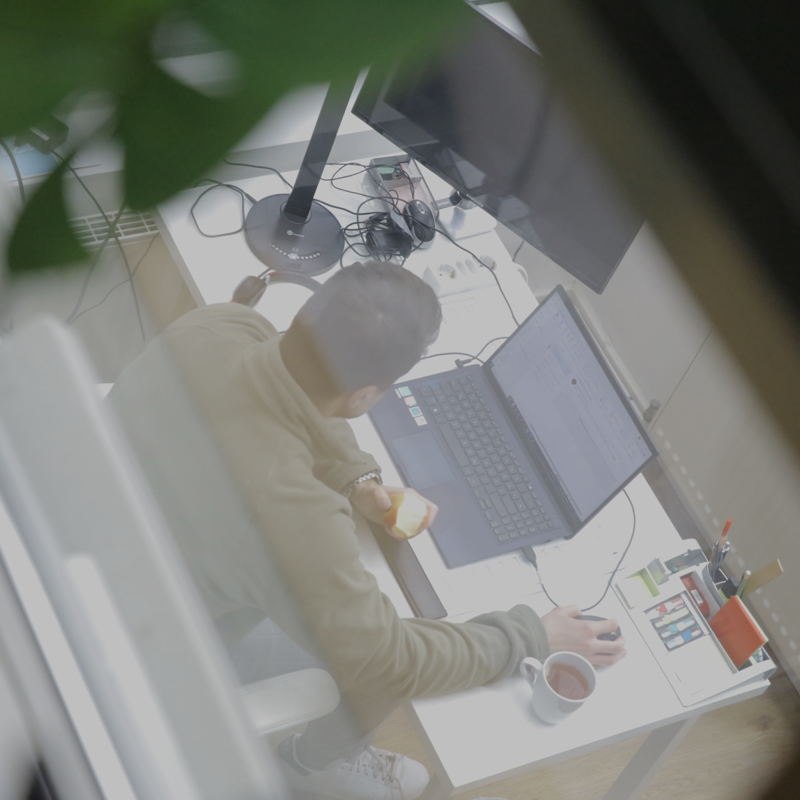 Person arbeitet an einem Laptop am Schreibtisch im Büro, hält einen Apfel in der Hand, aufgenommen aus erhöhter Perspektive