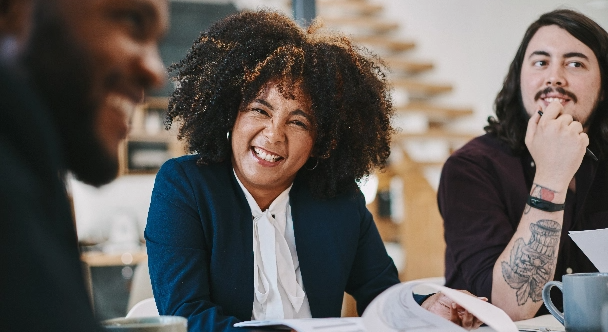 Eine Geschäftsfrau, die glücklich aussieht, während sie mit Kollegen im Sitzungssaal sitzt.