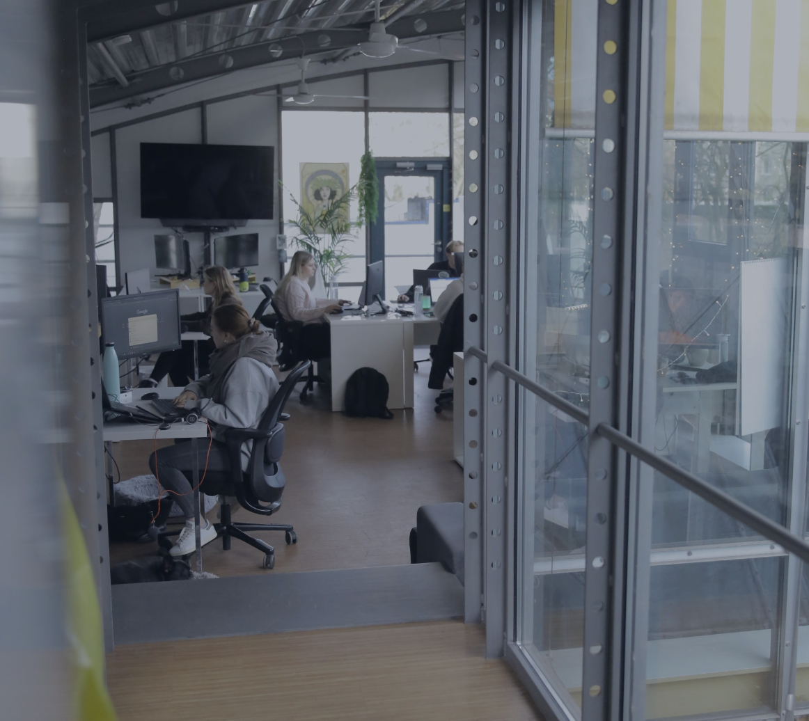 Blick durch eine Glaswand in ein Büro, in dem mehrere Personen an Schreibtischen arbeiten.