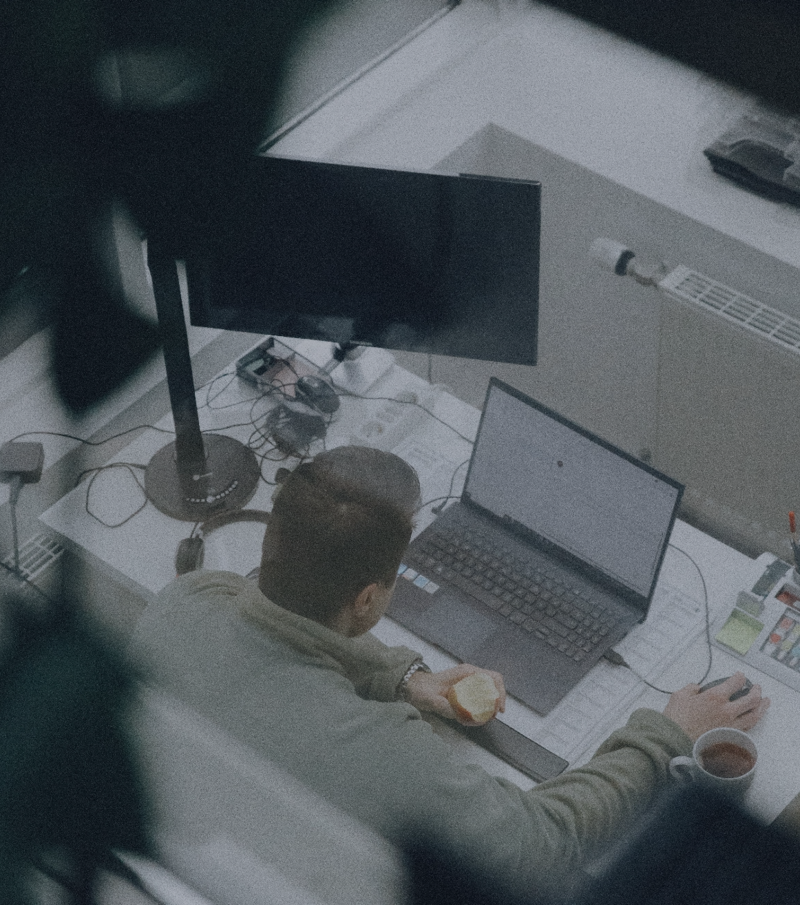 Person arbeitet an einem Laptop am Schreibtisch im Büro, hält einen Apfel in der Hand, aufgenommen aus erhöhter Perspektive