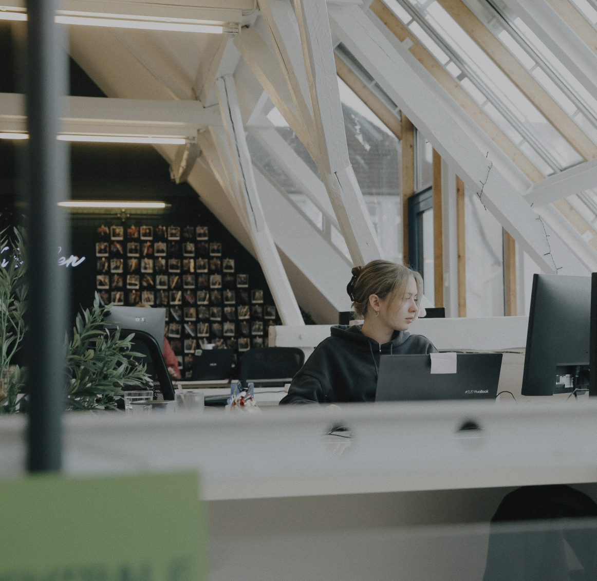 Person arbeitet konzentriert an einem Laptop in einem hellen Büro mit schrägen Dachfenstern und Holzbalken
