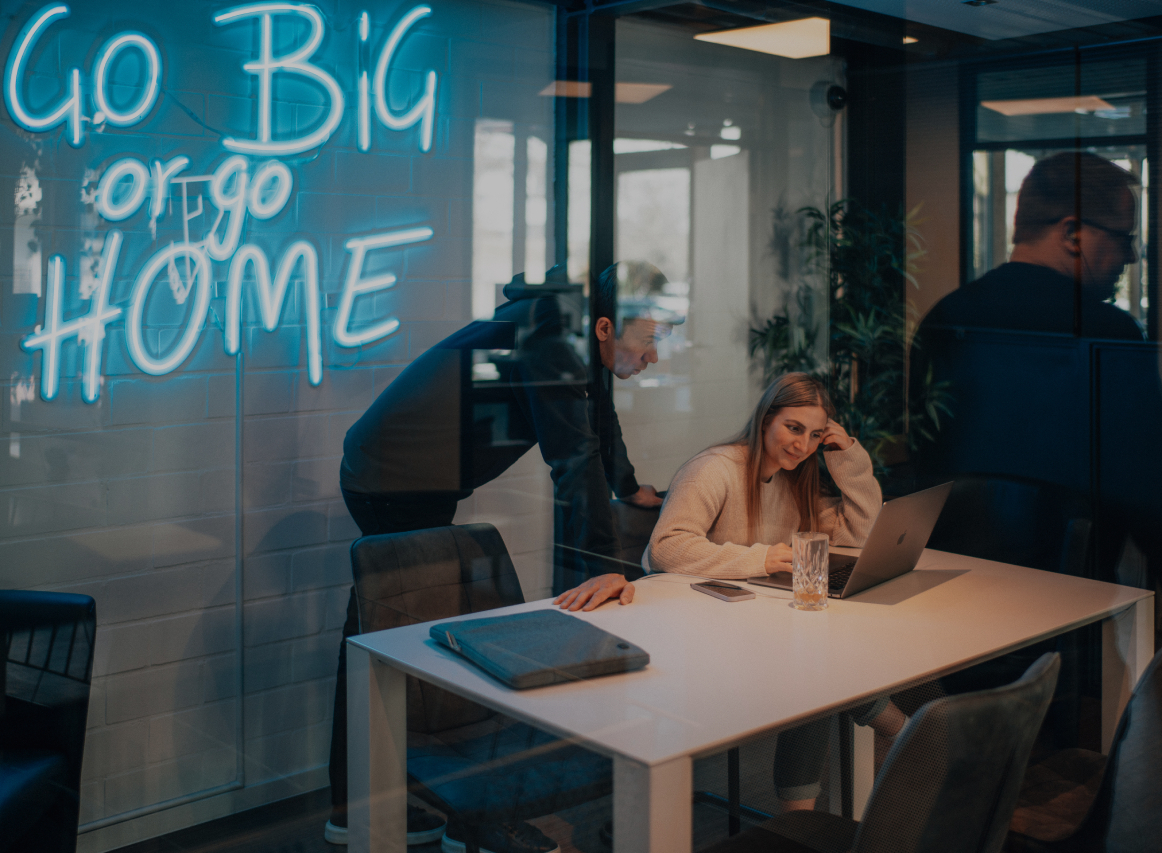 Zwei Personen arbeiten gemeinsam an einem Laptop in einem modernen Besprechungsraum, durch eine Glaswand fotografiert