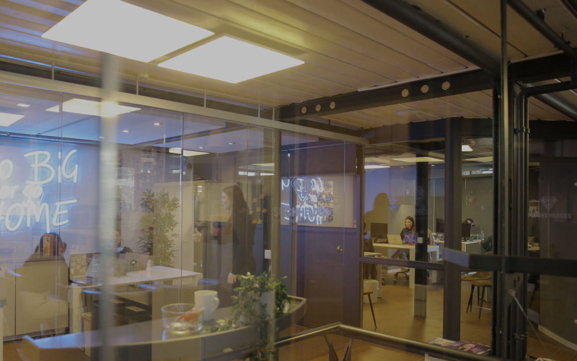 Fotografiert durch Glaswände in ein modernes Büro mit Besprechungsraum und arbeitenden Personen im Hintergrund.