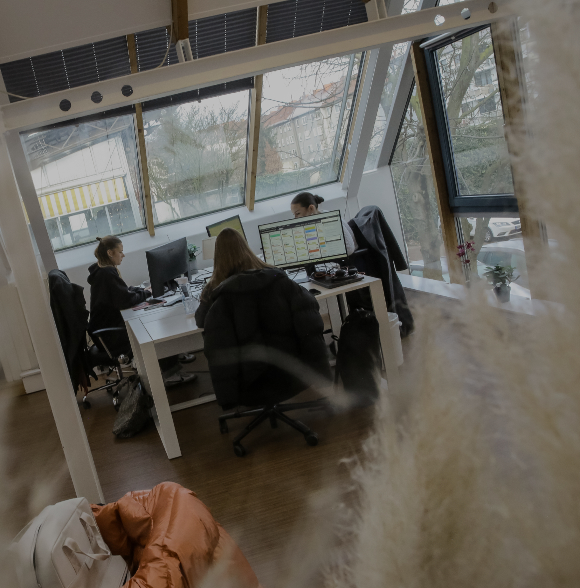 Person arbeitet an einem Schreibtisch im Büro, seitlich durch eine Glaswand fotografiert, mit Fensterfront im Hintergrund.