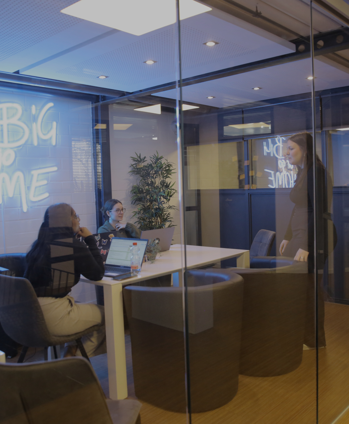 Blick durch Glaswände in ein modernes Büro mit Besprechungsraum und arbeitenden Personen im Hintergrund