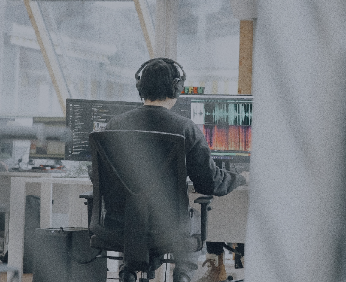 Person mit Kopfhörern arbeitet an einem Laptop im Büro, von hinten aufgenommen.