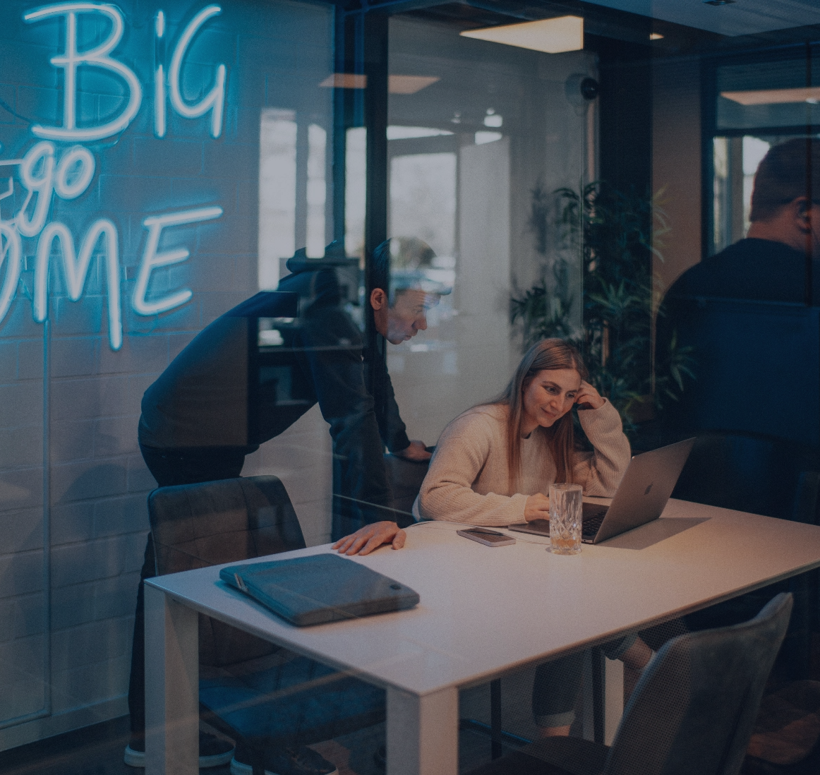 Zwei Personen arbeiten gemeinsam an einem Laptop in einem modernen Besprechungsraum, durch eine Glaswand fotografiert