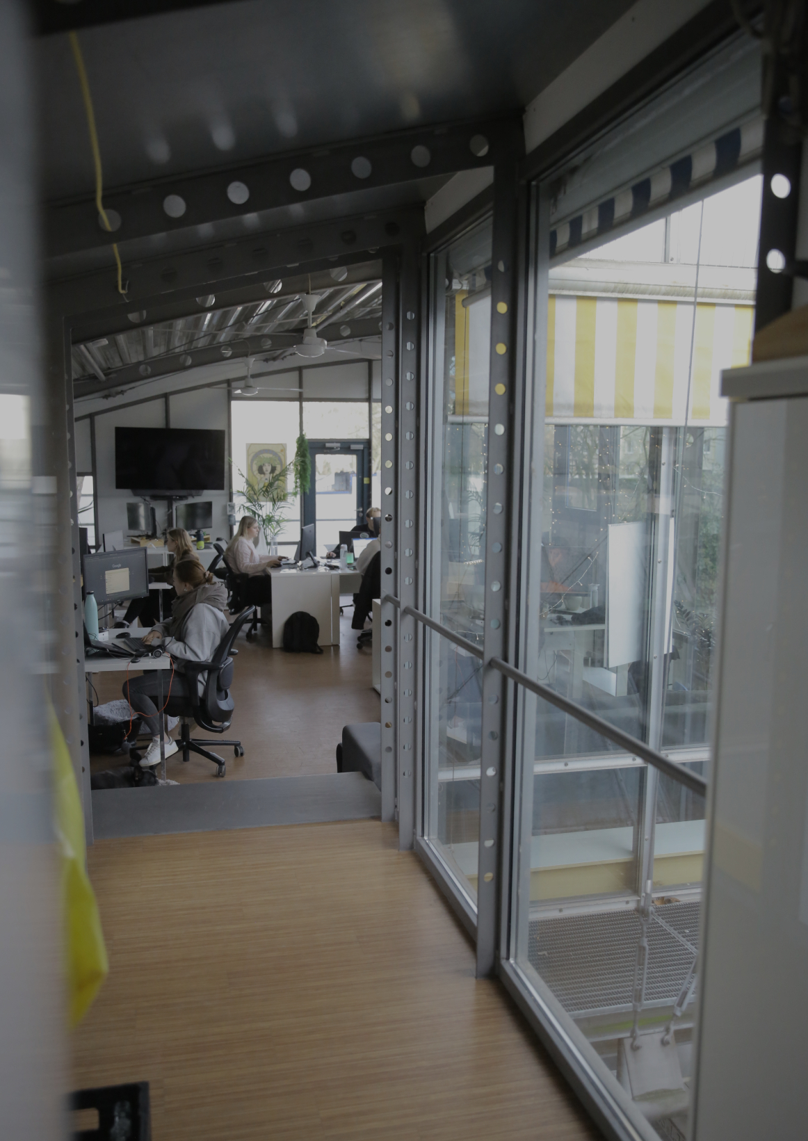 Blick durch eine Glaswand in ein Büro, in dem mehrere Personen an Schreibtischen arbeiten.