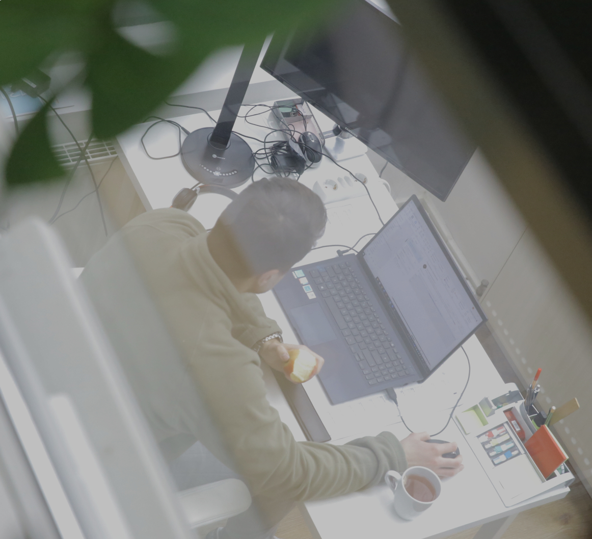 Person arbeitet an einem Laptop am Schreibtisch im Büro, hält einen Apfel in der Hand, aufgenommen aus erhöhter Perspektive