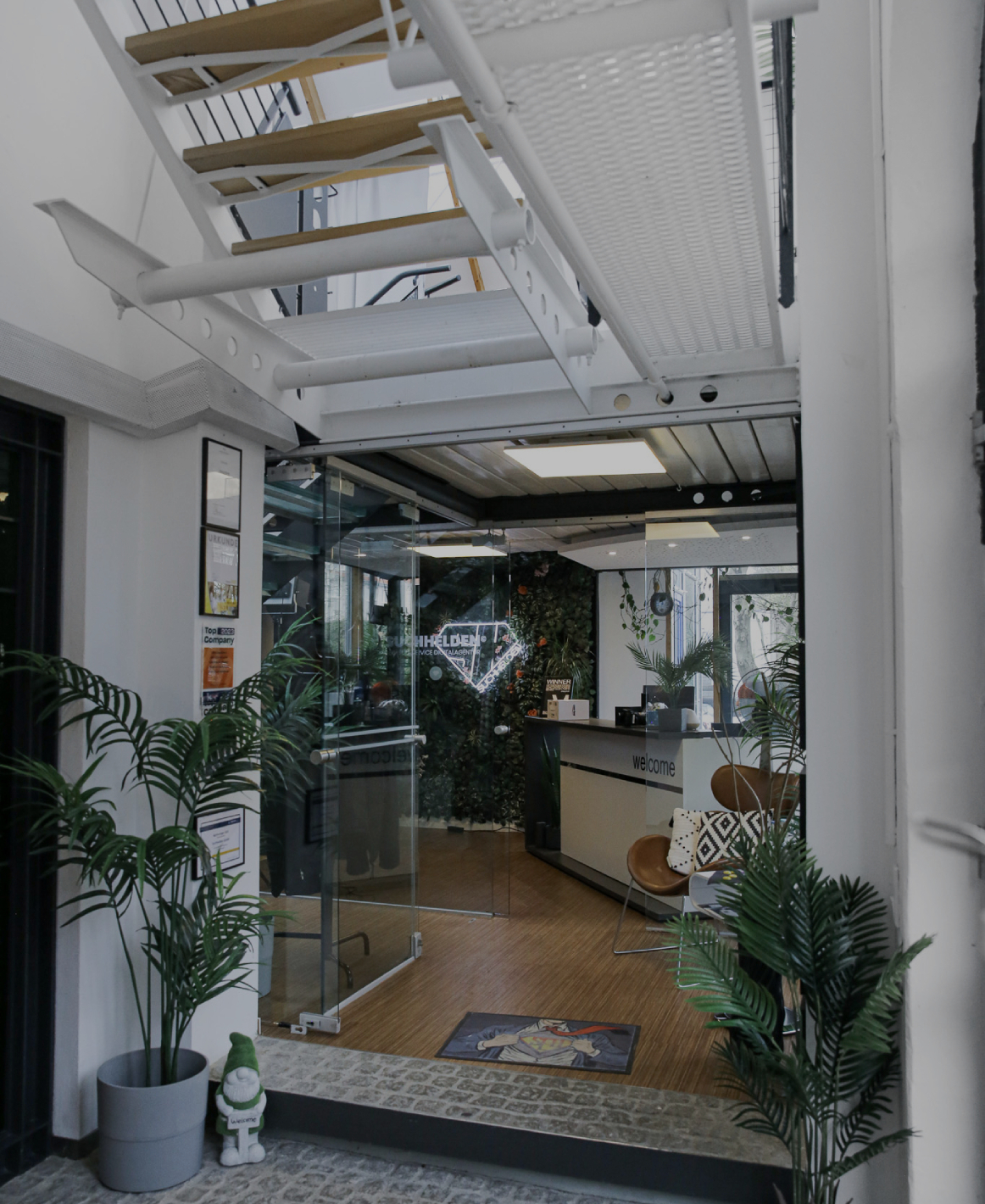 Eingangsbereich eines modernen Bürogebäudes mit Glas_tür, Empfangstresen, Pflanzen und offener Treppenkonstruktion
