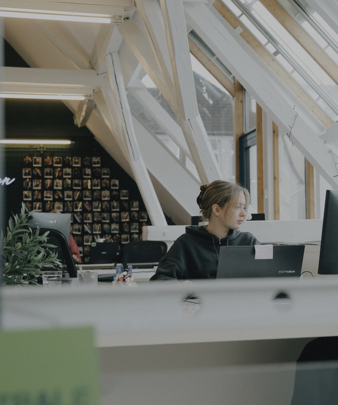 Person arbeitet konzentriert an einem Laptop in einem hellen Büro mit schrägen Dachfenstern und Holzbalken