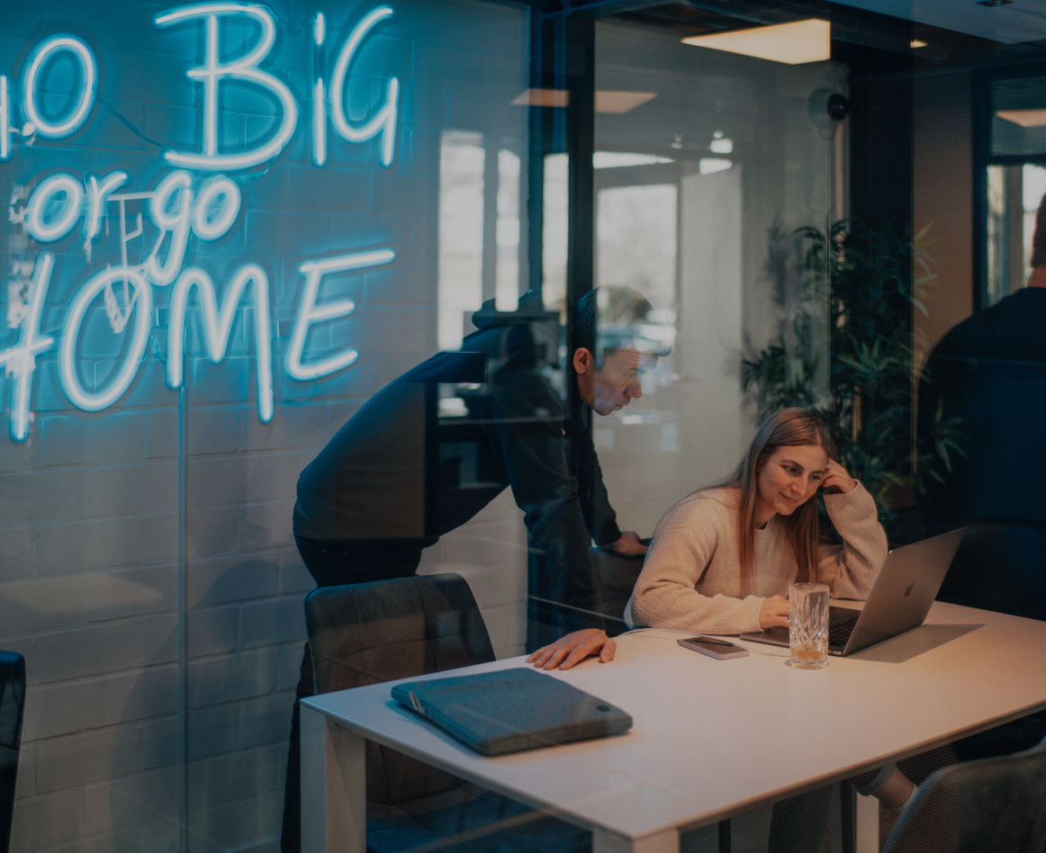 Zwei Personen arbeiten gemeinsam an einem Laptop in einem modernen Besprechungsraum, durch eine Glaswand fotografiert