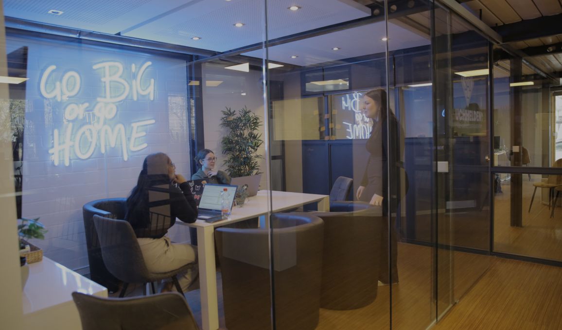 Blick durch Glaswände in ein modernes Büro mit Besprechungsraum und arbeitenden Personen im Hintergrund