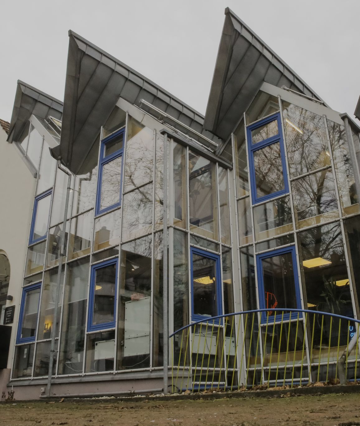 Aussenansicht eines modernen Glasgebäudes mit blauen Fensterrahmen und schrägem Dach 