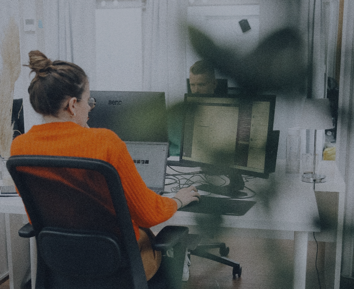 Mitarbeiterin sitzt an einem Schreibtisch im Büro und arbeitet am Computer mit mehreren Bildschirmen.