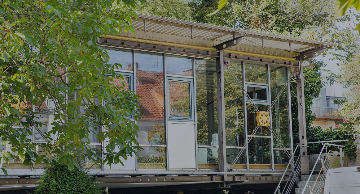 Modernes Bürogebäude mit großer Glasfassade, umgeben von Bäumen und Grünflächen