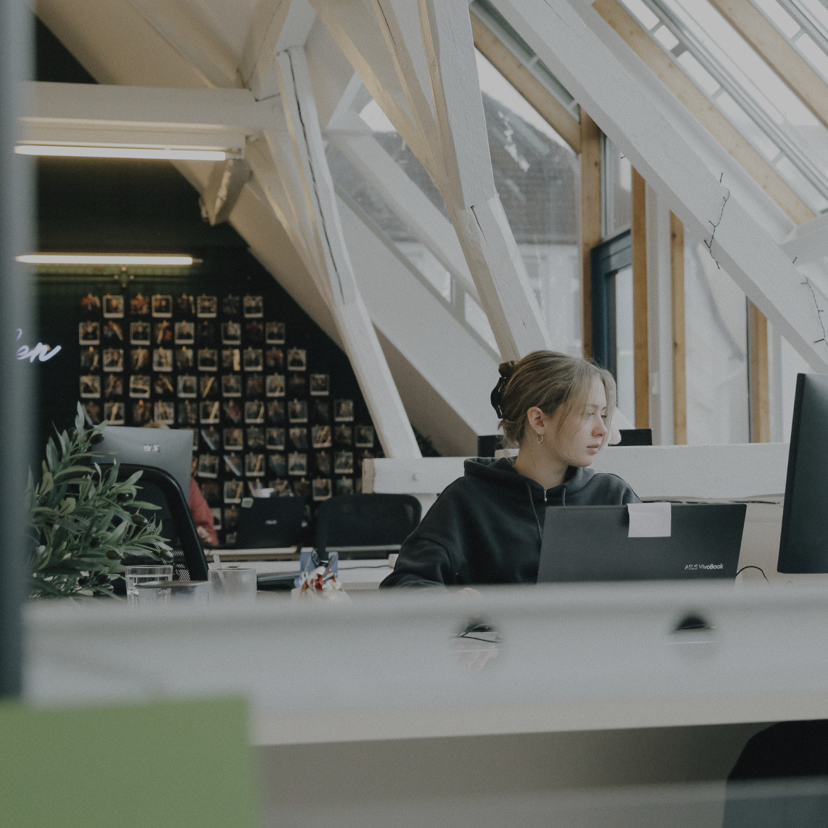 Person arbeitet konzentriert an einem Laptop in einem hellen Büro mit schrägen Dachfenstern und Holzbalken