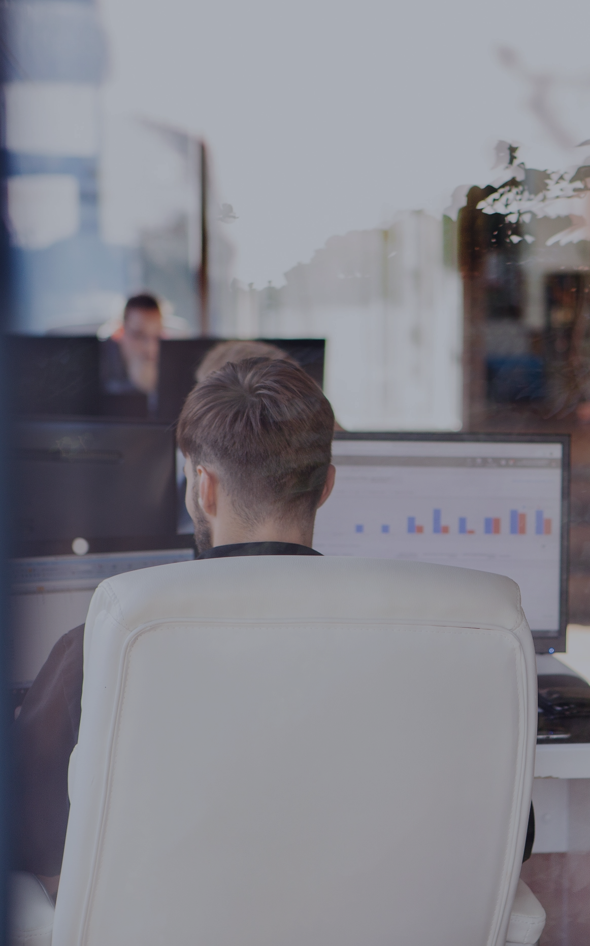 Mehrere Personen arbeiten an Computern in einem lichtdurchfluteten Büro mit großen Fenstern und Pflanzen.