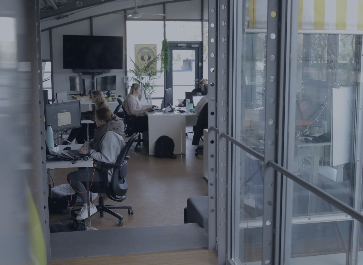 Blick durch eine Glaswand in ein Büro, in dem mehrere Personen an Schreibtischen arbeiten.