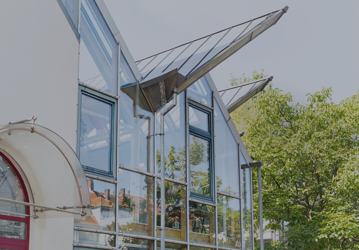 Außenansicht eines modernen Bürogebäudes mit Glasfassade, großen Fenstern und Bäumen im Vordergrund.