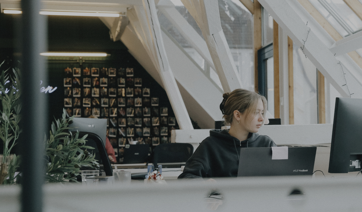 Person arbeitet konzentriert an einem Laptop in einem hellen Büro mit schrägen Dachfenstern und Holzbalken
