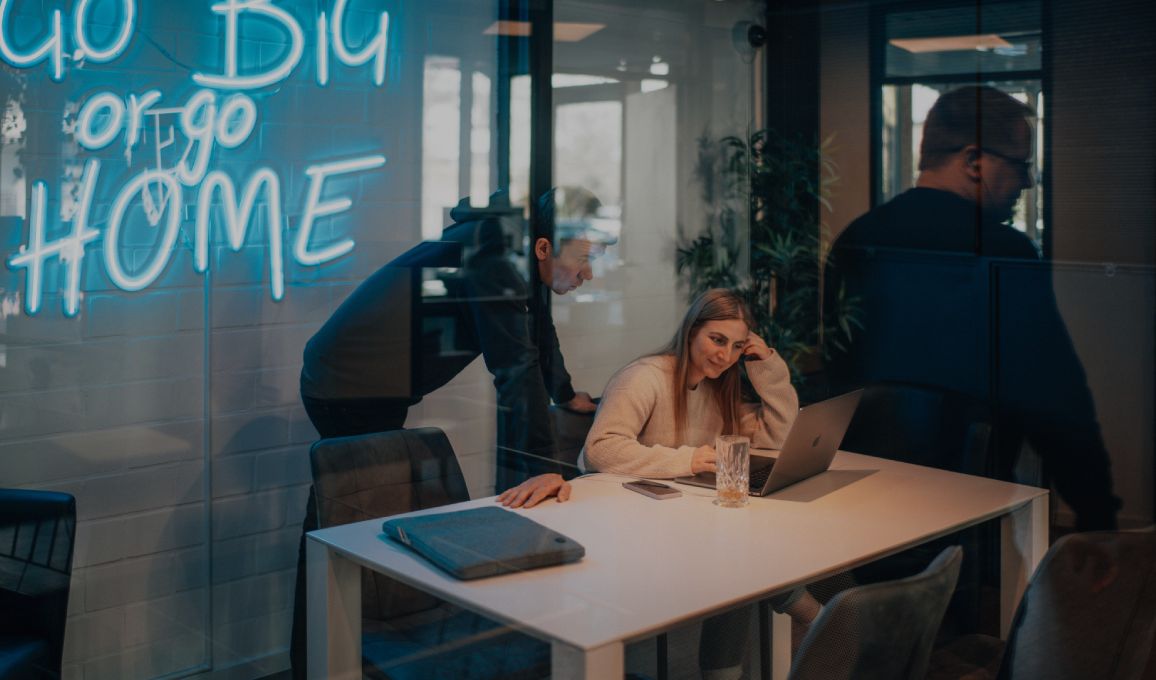 Zwei Personen arbeiten gemeinsam an einem Laptop in einem modernen Besprechungsraum, durch eine Glaswand fotografiert
