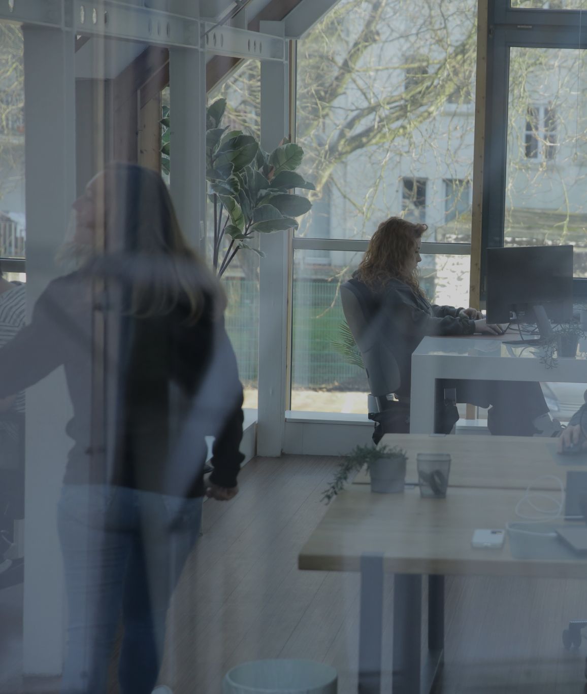 Person arbeitet an einem Schreibtisch im Büro, seitlich durch eine Glaswand fotografiert