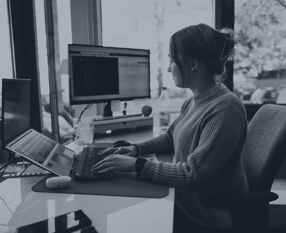 Person arbeitet am Laptop an einem Schreibtisch mit zusätzlichem Monitor im Hintergrund