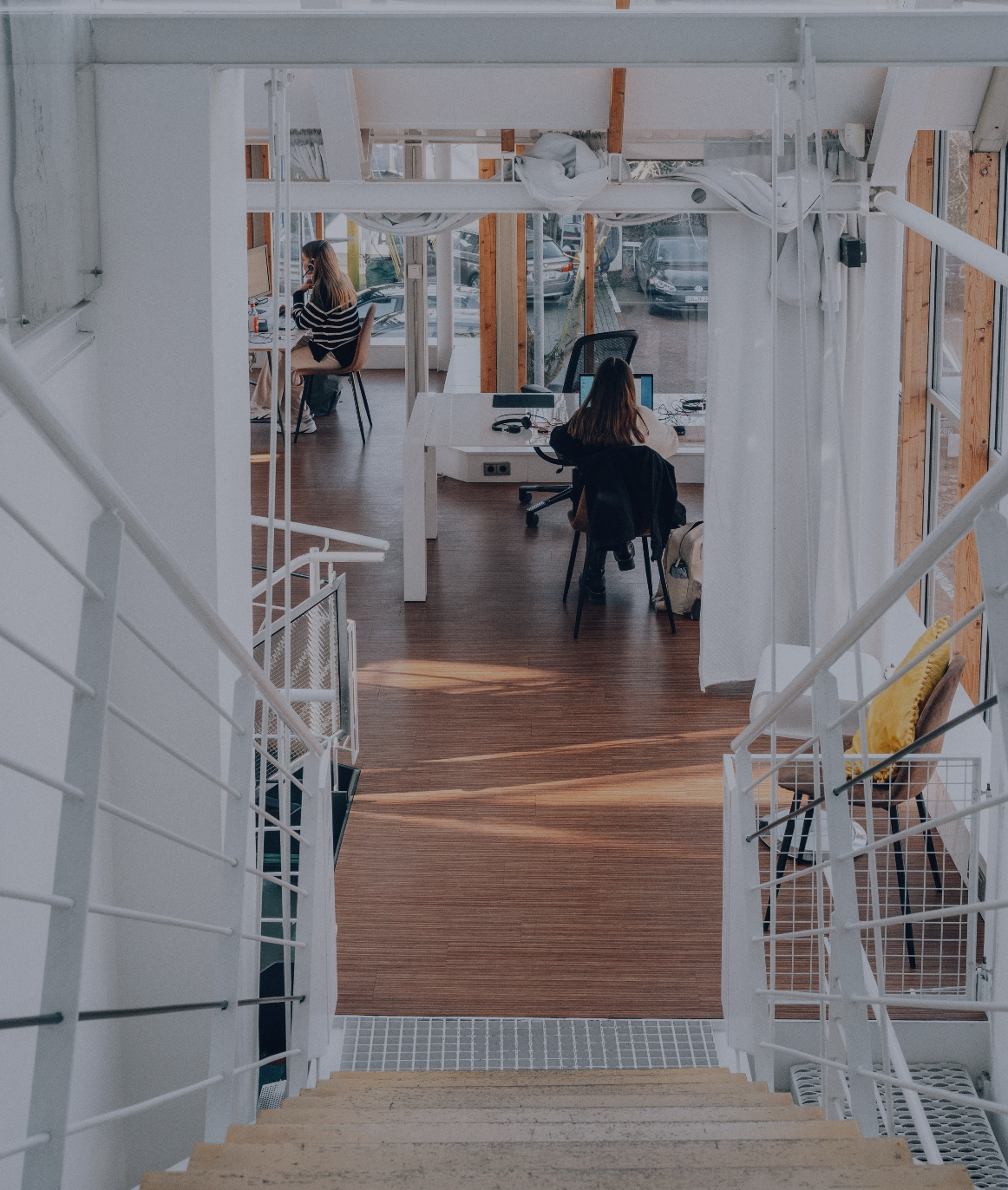 Blick von einer Treppe in ein helles Büro mit zwei Personen an Schreibtischen