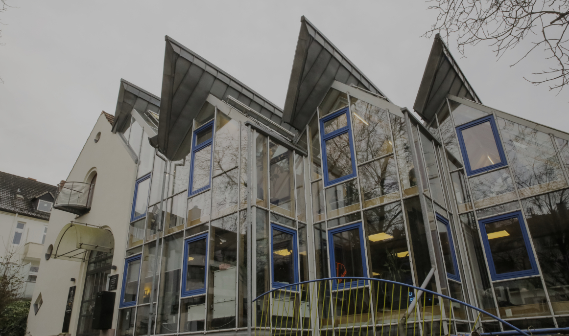 Aussenansicht eines modernen Glasgebäudes mit blauen Fensterrahmen und schrägem Dach