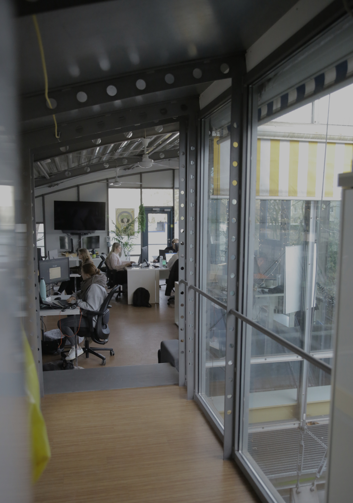 Blick durch eine Glaswand in ein Büro, in dem mehrere Personen an Schreibtischen arbeiten.