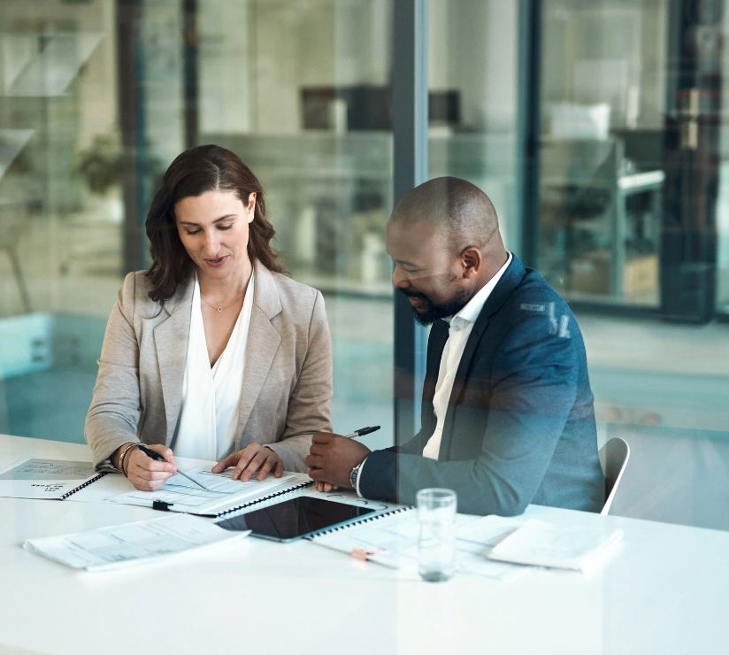Mann und Frau sitzen in einem modernen Büro in einem Besprächungsraum und schauen sich Dokumente an 