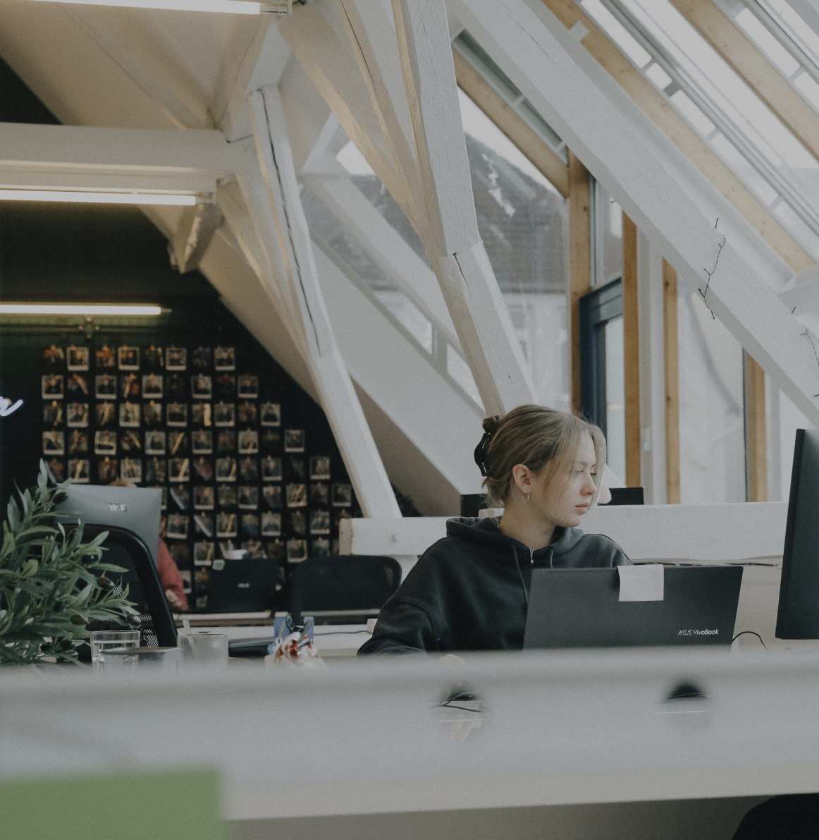 Person arbeitet konzentriert an einem Laptop in einem hellen Büro mit schrägen Dachfenstern und Holzbalken
