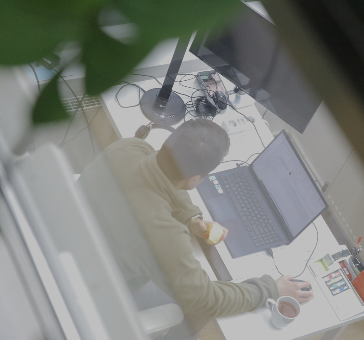 Person arbeitet an einem Laptop am Schreibtisch im Büro, hält einen Apfel in der Hand, aufgenommen aus erhöhter Perspektive